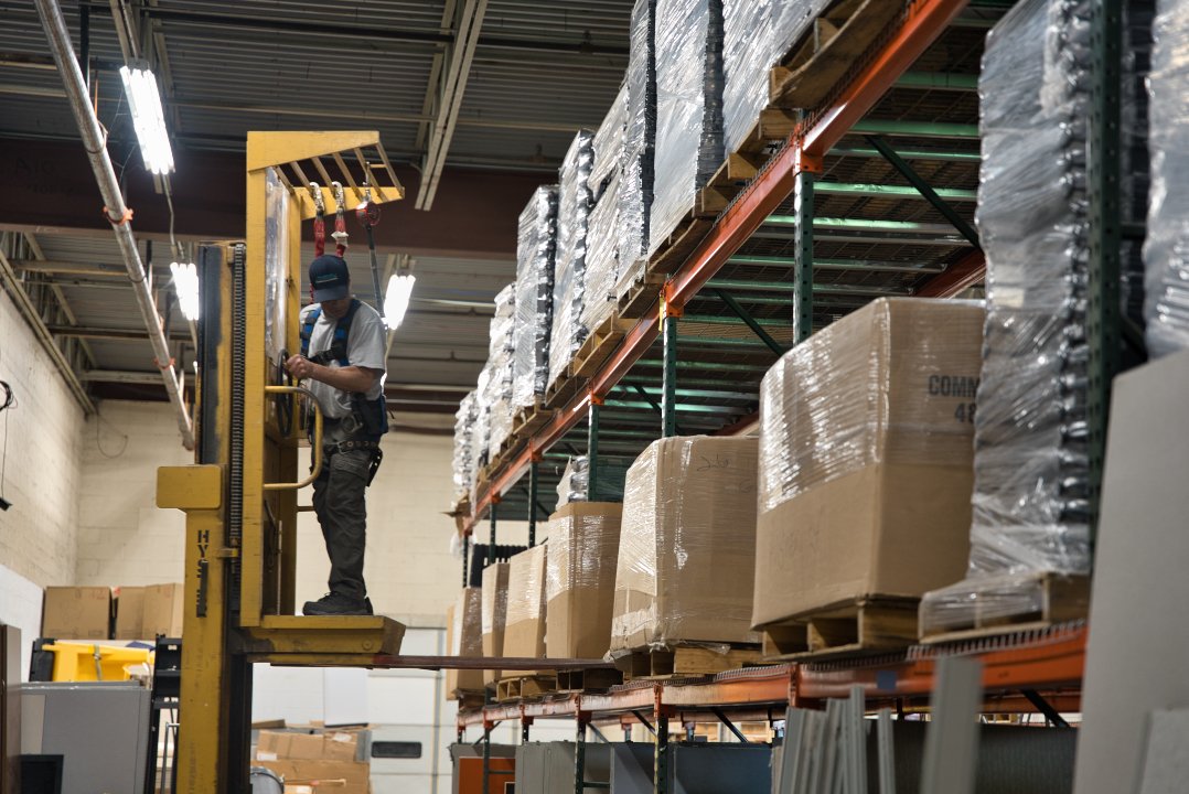 Warehouse associate operating lifting equipment to safely store and organize commercial office furniture inventory for warehousing, distribution, and staged delivery projects